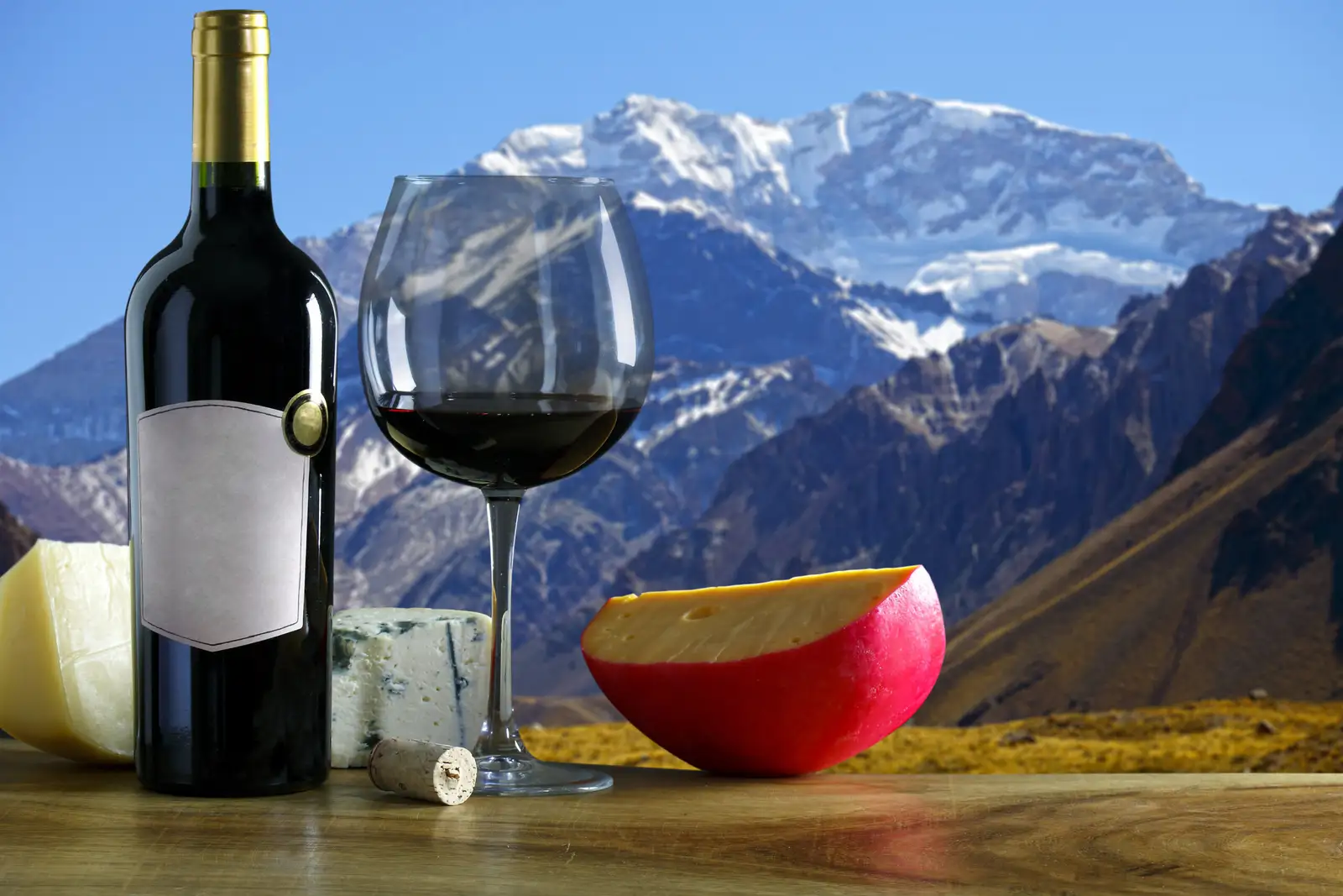 A bottle and a glass of red wine, with the Andes behind